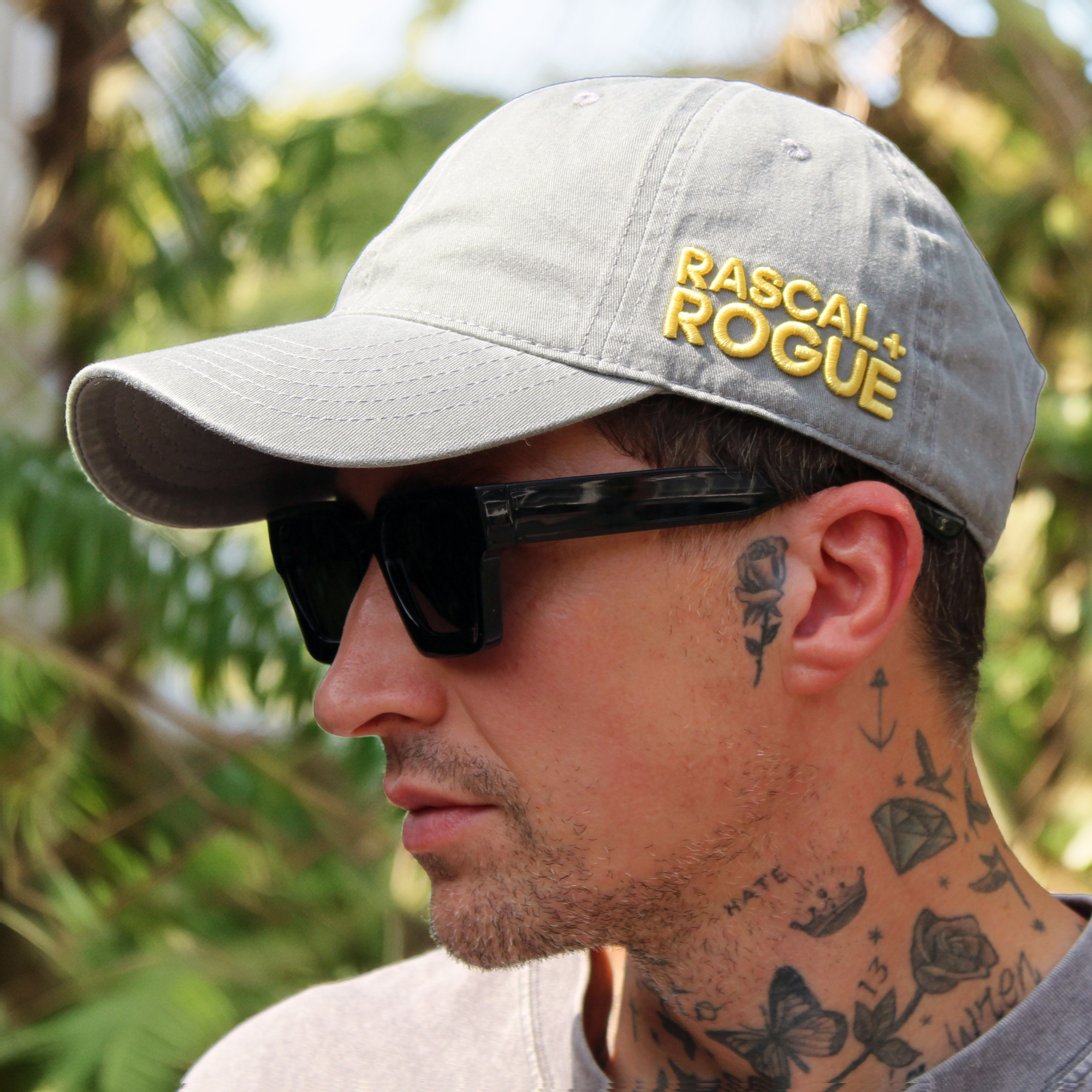 Man wearing a cap with 'Rascal Rogue' logo and sunglasses, outdoors.