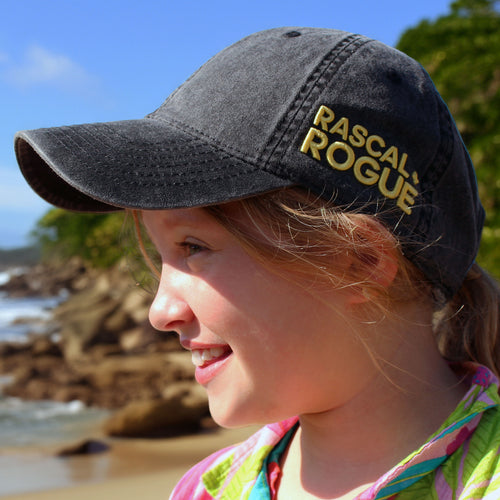 Child wearing a 'Rascal Rogue' cap on a beach