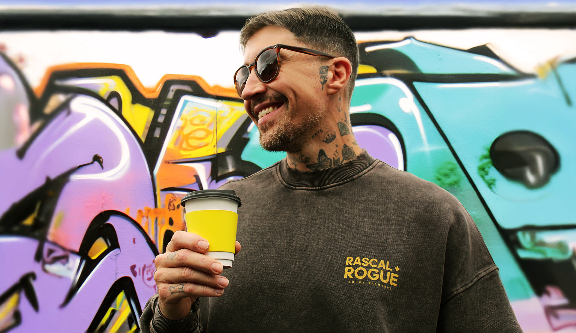 Man holding a yellow cup with graffiti art in the background
